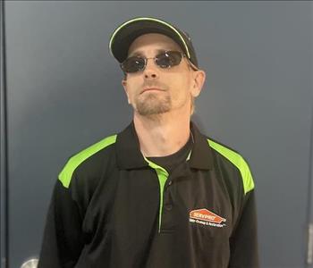 Male in black SERVPRO shirt and prescription glasses in front of blue/grey background.